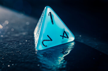 Close-up of a single blue four sided dice on a wet slate surface