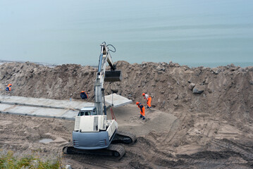 Russia, the city Zelenogradsk - 25.10.2020. Fortifying the beach, a Terex excavator works on the beach. Workers dismantle the old fortifications that held the slope. Equipment and workers fill a new c