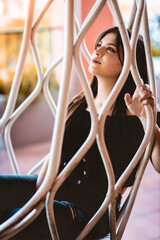 chica morena guapa pensativa posando vestida de negro sentada en silla colgante de madera