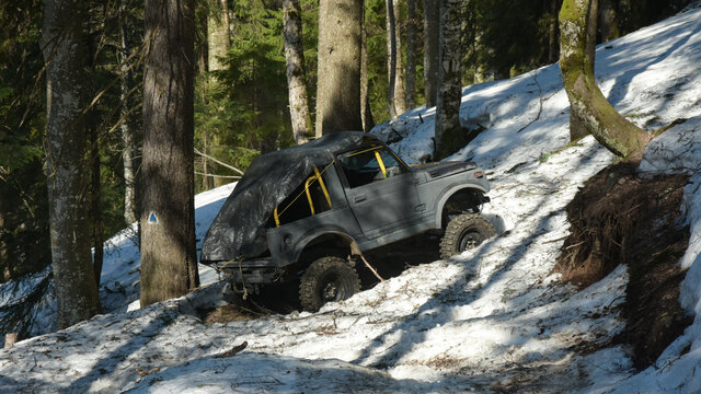 An abandoned extreme off road vehicle laying into the middle of the forest. Spring season, snow is still covering the land.