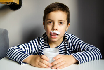 Boy in striped t-shirt with a mustache from kefir or milk in the grey background and glass in  his...