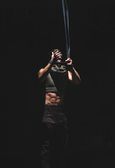 Muscular acrobat in the dark prepares ropes for an exercise.