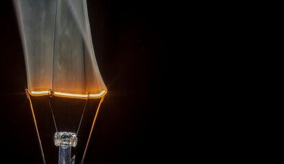 Filament light bulb on fire and smoking, isolated black background. Copy space for text.