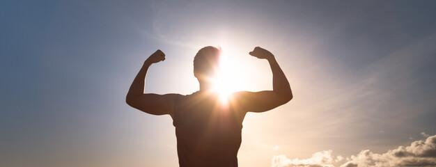Strong man flexing against sunset sky 