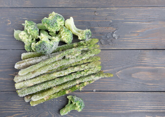 Frozen asparagus and broccoli on a wooden surface with space for text. Article, recipe.