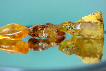 A piece of natural amber on a mirror surface, a reflection of a yellow semi-precious stone