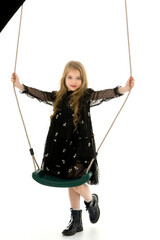 Cute little girl is standing near the swing.