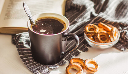 Hot steaming coffee in a black Cup, cookies and an old book on a white wooden table