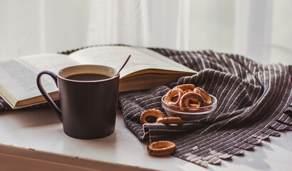 Hot steaming coffee in a black Cup, cookies and an old book on a white wooden table