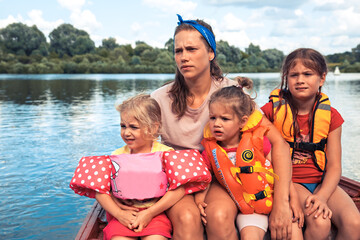 Children in life jackets together with mother floating on boat on river countryside outdoors as big...