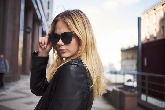 Fashionable woman in a leather jacket and sunglasses near the building 