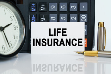 On the table there is a clock, a pen, a calculator and a business card on which the text is written - LIFE INSURANCE