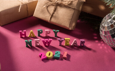 Happy New Year greeting words made of wooden letters, gift boxes on a purple background decorated with festive tree branches.