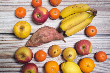 Many orange and yellow autumn fruits like apples, mandarins, pears and bananas on a wooden table
