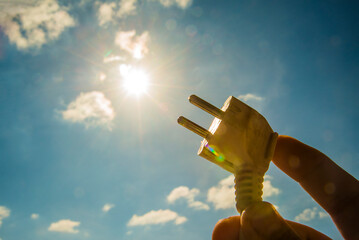 symbolic solar energy theme showing the sun and sky with human hand holding a electrical socket...