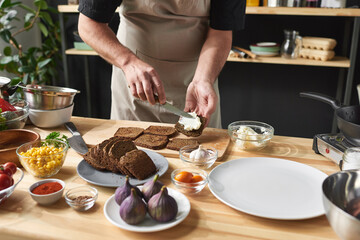 Close-up of chef in apron putting butter on bread he preparing toasters at the table in the kitchen