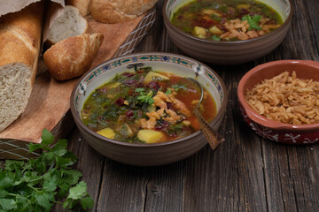 Beet greens and potato soup with bread and crispy onion, wooden background