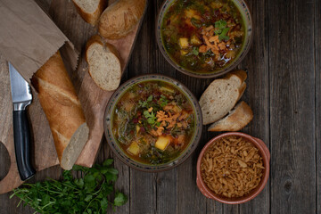 Beet greens and potato soup with bread and crispy onion, wooden background