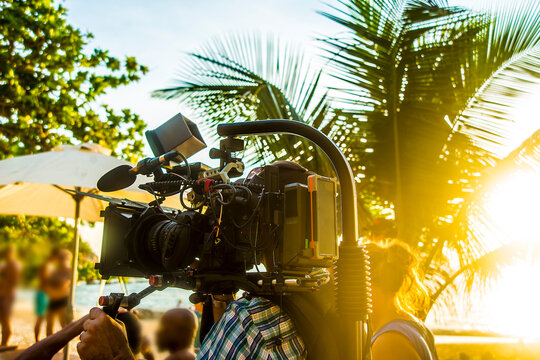 Beach Video Making, Prefessional Videographer Taking Video Of Young People At Summer Beach Party. Sunny Tropical Day. Sun Rays Beam