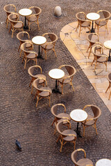 An empty outdoor French cafe with white tables and rattan chairs in the early morning, seen from above in the city of Nimes. Vertical view