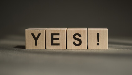 A wooden blocks with the word YES written on it on a gray background. Business concept
