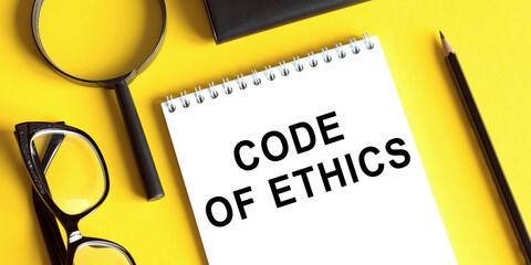 Notepad with the text Code of Ethics on a yellow background with glasses, a magnifying glass and a pencil. Business concept.