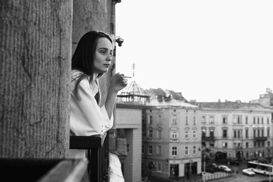 Black and white photo, young pretty girl smoking on the balcony, morning sunrise, not a healthy lifestyle