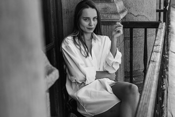 Black and white photo, young pretty girl smoking on the balcony, morning sunrise, not a healthy lifestyle