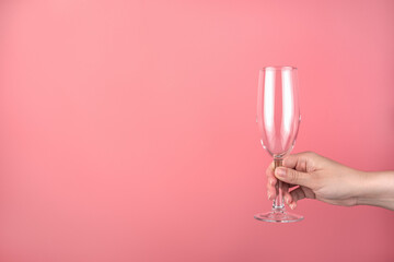 Hand holding an empty champagne glass on a pink background. Side view with space for copying. Concept of holiday backgrounds. © Helga1