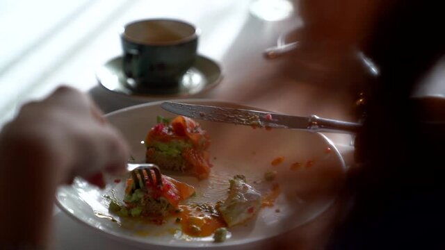 woman is eating meal with salmon and vegetables in restaurant, closeup of her plate, using fork and knife