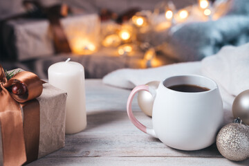 Cozy Christmas background with Cup, gift, candles on the background of burning lights. Side view. The concept of Christmas and the New year.