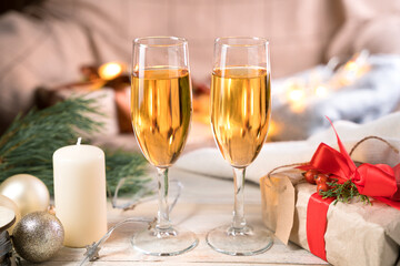 Two glasses of champagne, a gift and a candle on the table in a Christmas atmosphere. The view from the side. Concept of holiday backgrounds.