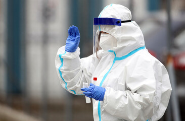Medical staff member with mask and protective equipment gestures as performs Coronavirus nasal...