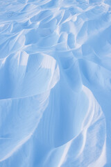 Fototapeta premium Snow texture. Wind sculpted patterns on snow surface. Wind in the tundra and in the mountains on the surface of the snow sculpts patterns and ridges (sastrugi). Arctic, Polar region. Winter background