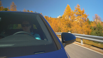 Fototapeta na wymiar CLOSE UP: Young male tourist drives his blue car along a scenic mountain road