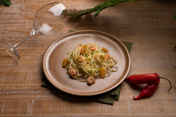 pasta dish with shrimp on wooden table with glass of wine and peppers