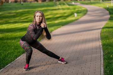 is professionally engaged in the low squat in the Park. portrait of a sporty female sports coach of Caucasian appearance brown-haired in comfortable clothes. aerobics training fitness training.