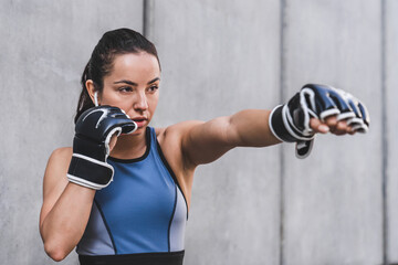 Attractive young female athlete practicing with boxing gloves in the grey wall background