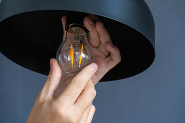 Close-up. A hand changes a light bulb in a stylish loft lamp. Spiral filament lamp. Modern interior decor.