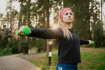 Confident woman training in the park uses dumbbells