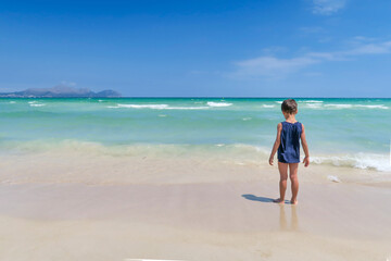child with his back to the sea of turquoise water on the beach of Muro, Palma de Mallorca, Spain, Mediterranean Sea