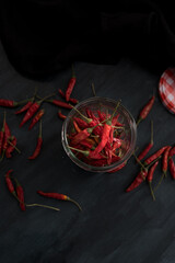 Overhead view focused on a vertical transparent jar full of red chili peppers. More blurred peppers are around the jar on a wooden rustic background.
