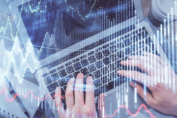 Double exposure of man's hands typing over computer keyboard and forex graph hologram drawing. Top view. Financial markets concept.