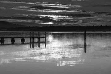 Clouds, reflections and sunrise over the bay in black and white