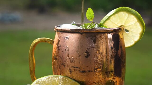 Pouring soda into a cocktail drink in a copper mug with lime and mint