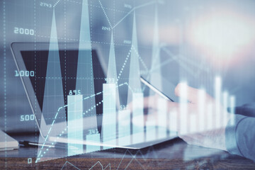 Double exposure of man's hands holding and using a digital device and forex graph drawing. Financial market concept.