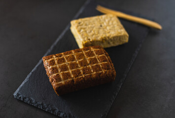 Two pieces of soy products. Smoked tofu and tempeh. Healthy protein foods on a slate board