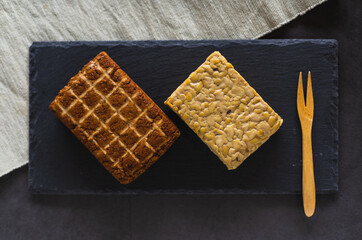 Top view of two pieces of soy products. Smoked tofu and tempeh. Healthy protein foods on a slate board