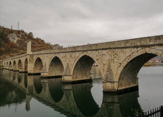 Fototapeta premium Beautiful old stone bridge with arches diagonnally over a river reflecting in the water, autumn scene