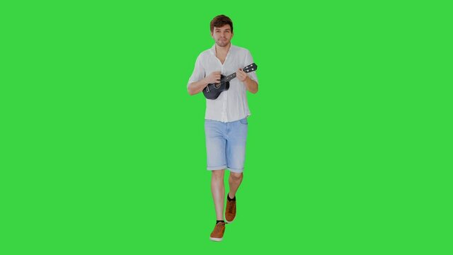 Young man playing ukulele while walking on a Green Screen, Chroma Key.